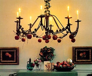 Christmas Chandelier. A magnificent, eight-branched, hanging candelabra is garlanded with rosy apples and larch cones. The flickering candles cast a welcoming light round the hall and are reflected in the shiny baubles.